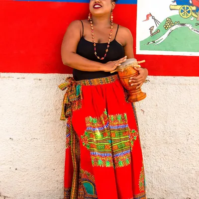 Femme en jupe dashiki devant le drapeau haïtien